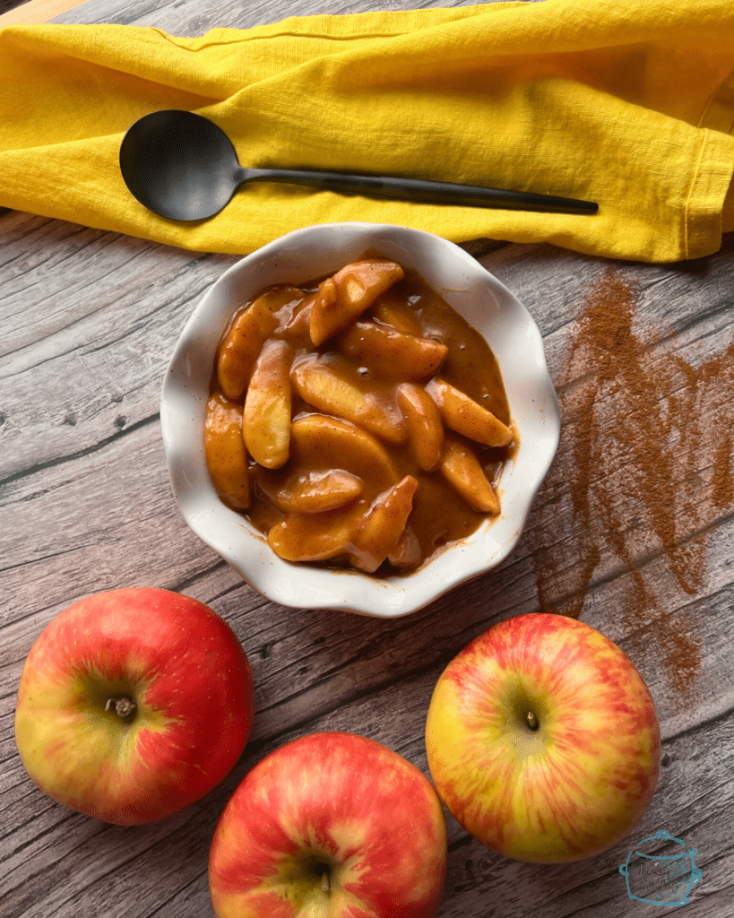 A white bowl filled with slow cooked caramel apple pie filling with a spoon on a yellow napkin