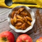 A white bowl filled with slow cooked caramel apple pie filling with a spoon on a yellow napkin
