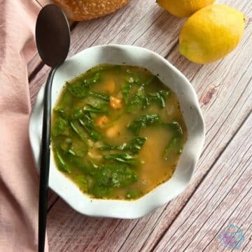 a white bowl of slow cooker white bean soup with a spoon, napkin and lemons