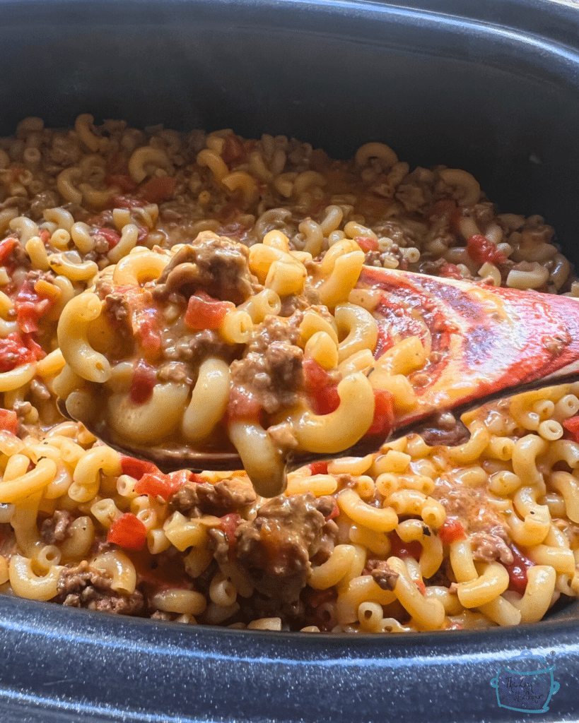 macaroni noodles with ground beef and sauce on a wooden spoon held over a crockpot