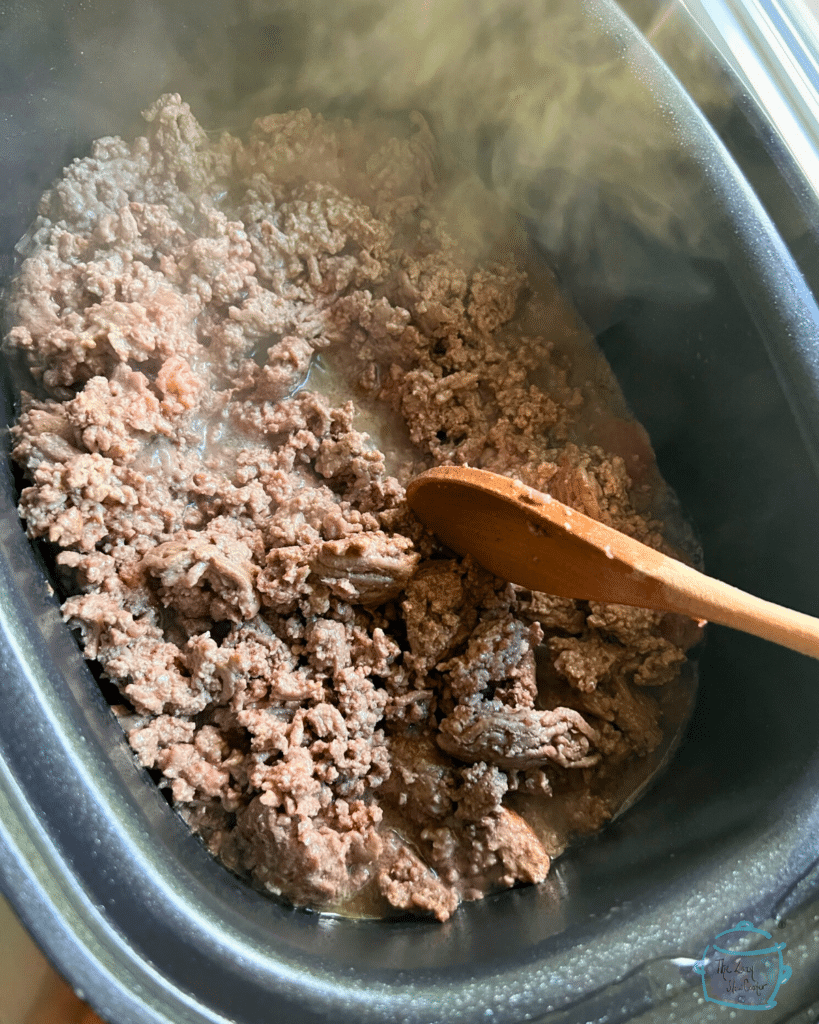 ground beef in a slow cooker being browned and stirred with a wooden spoon