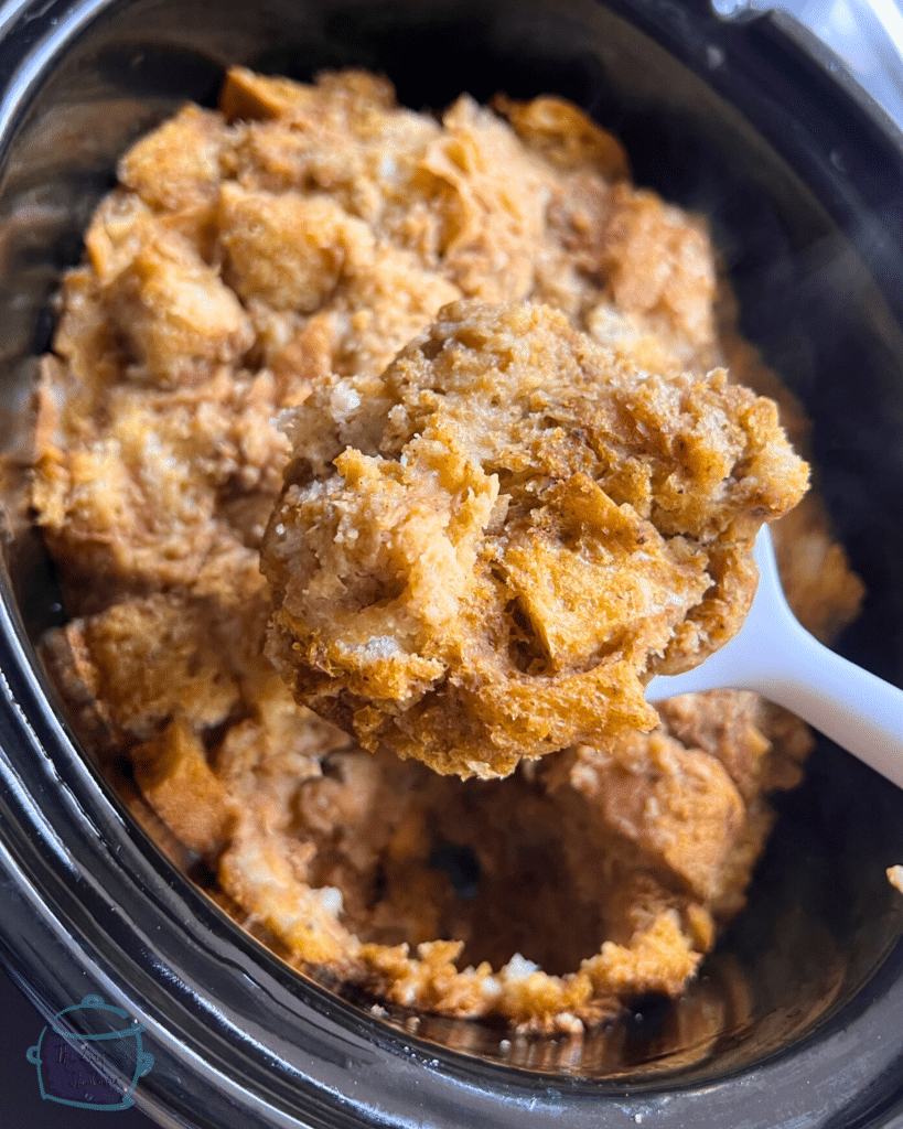 pumpkin bread pudding on a spoon over slow cooker full of the same