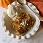 a serving of slow cooker bread pudding in a white bowl with a scoop of vanilla ice cream.