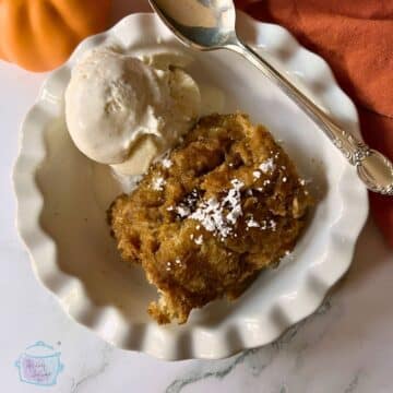 a serving of slow cooker bread pudding in a white bowl with a scoop of vanilla ice cream.