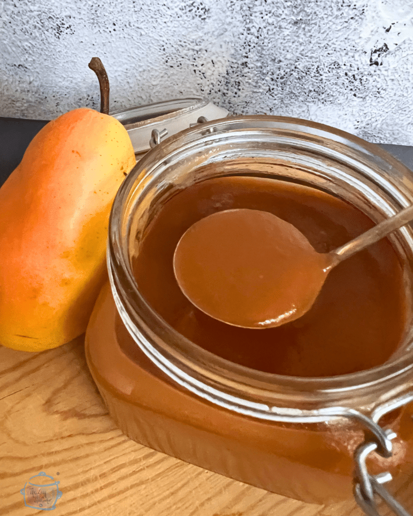 Slow cooker salted caramel pear butter in a jar with the lid off. A spoonful of the same held overtop