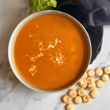 A bowl of slow cooker tomato and feta cheese soup with soup crackers off to the side.