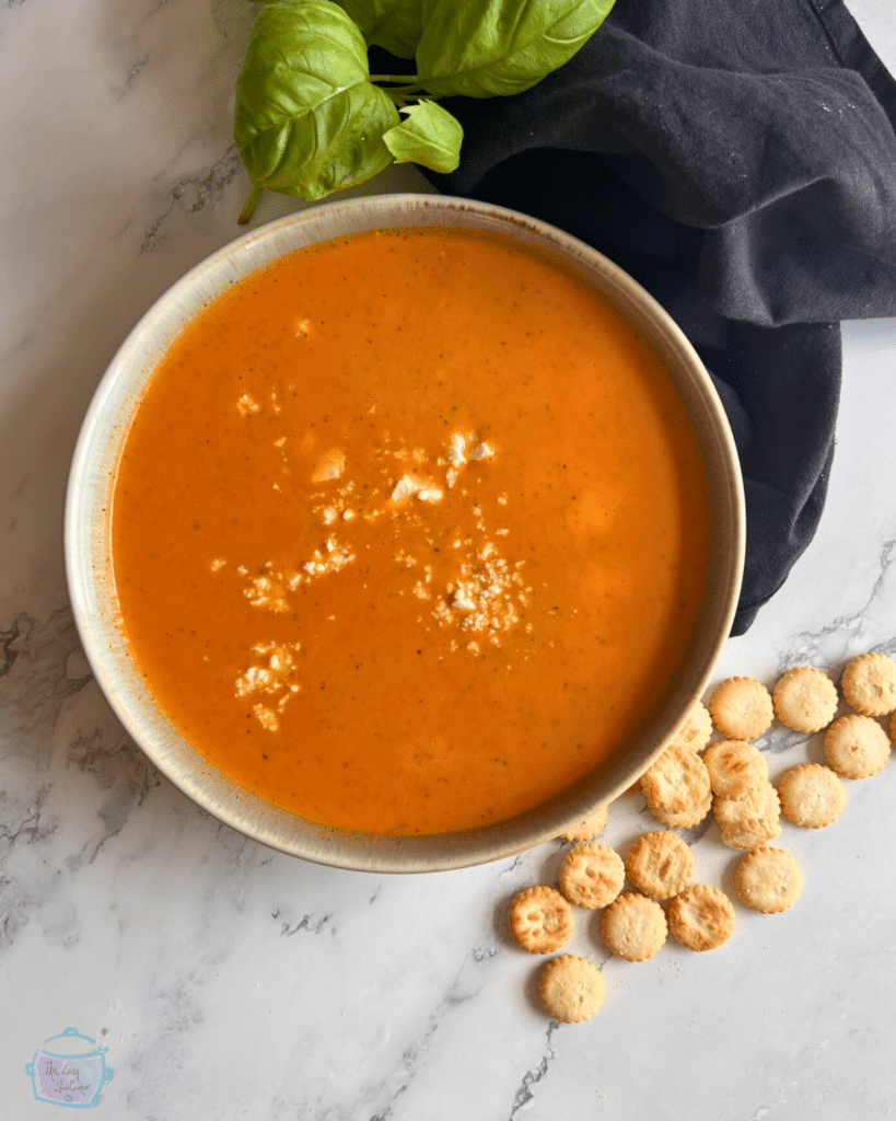 A bowl of slow cooker tomato and feta cheese soup with soup crackers off to the side.