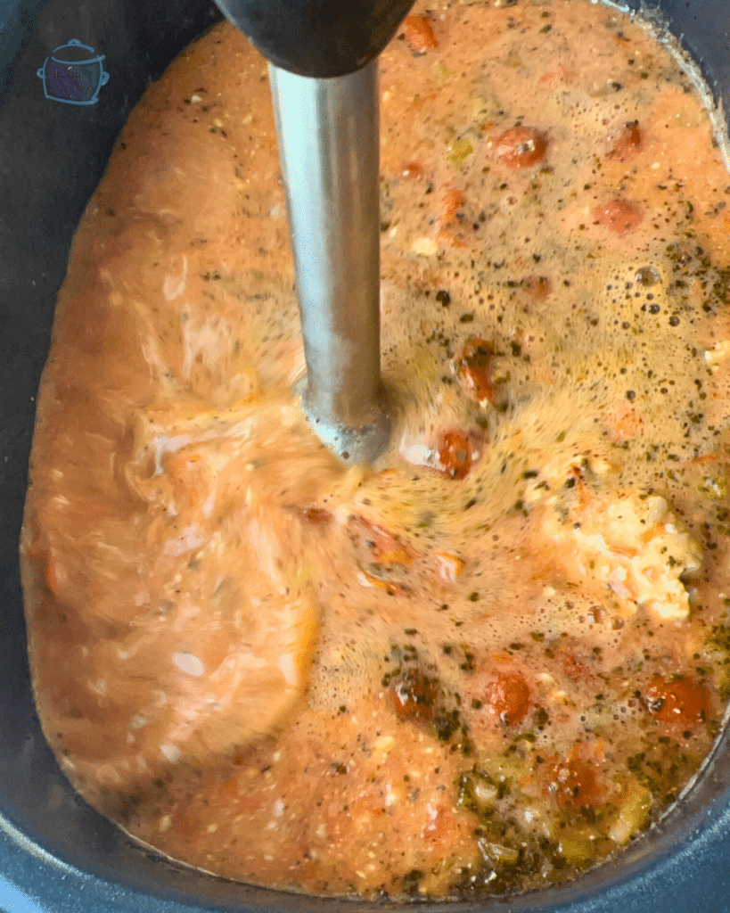 tomato and feta soup ingredients in a crockpot being blended with an immersion blender