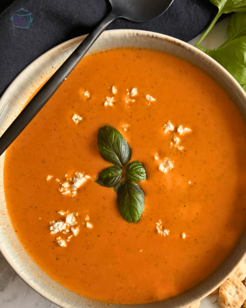 A bowl of slow cooker tomato and feta cheese soup with soup crackers off to the side.