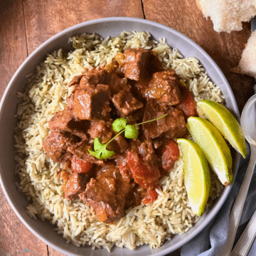 stewed beef on a bed of rice in a grey bowl with lime wedges on the side