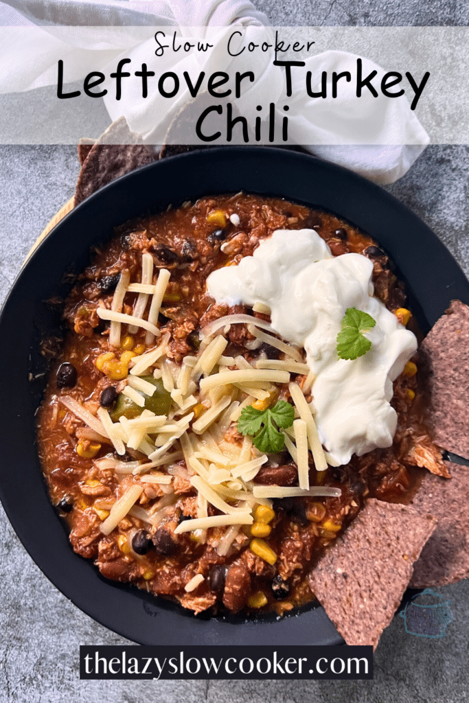 Turkey crockpot chili in a black bowl topped with shredded cheese and sour cream