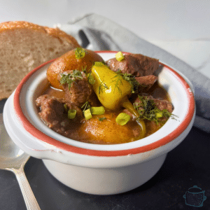 slow cooker beef stew with pepperoncini peppers in a round white bowl