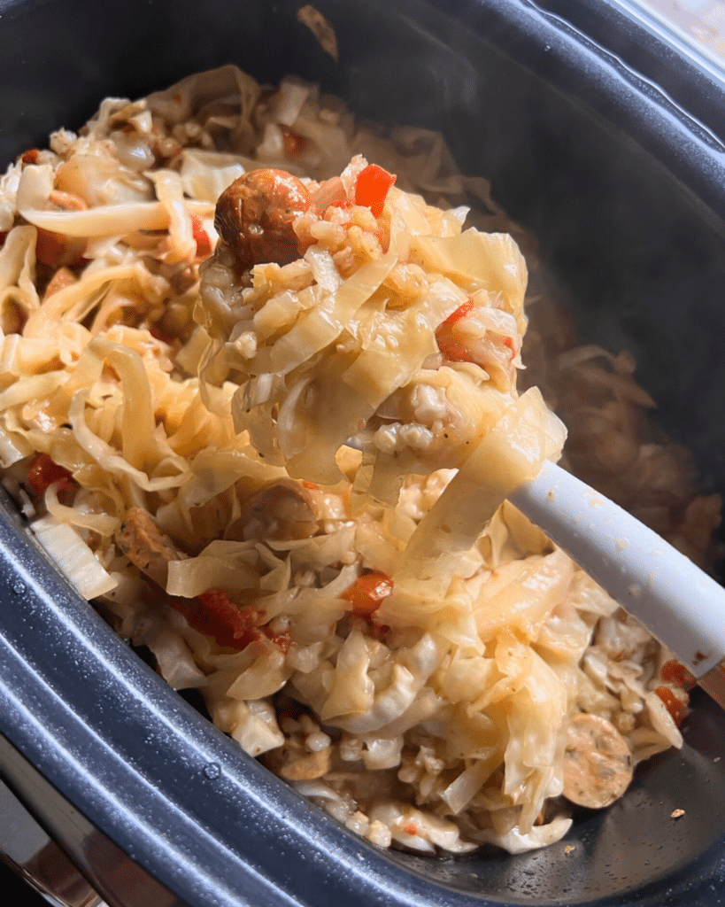cooked cabbage and sausage on a spoon held over a crockpot full of the same
