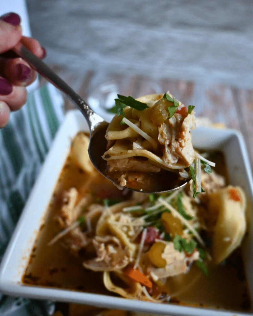 Crockpot ravioli soup on a spoon held over a bowl of the same