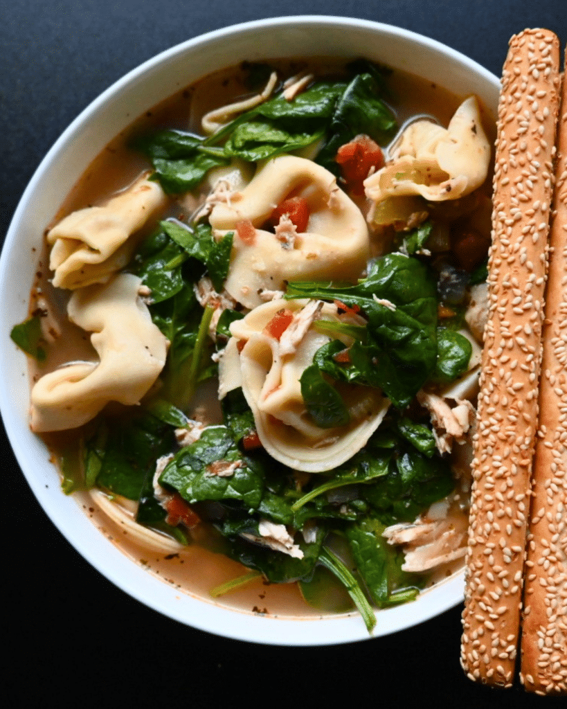 A close picture of chicken tortellini and spinach soup with sesame bread sticks on the side