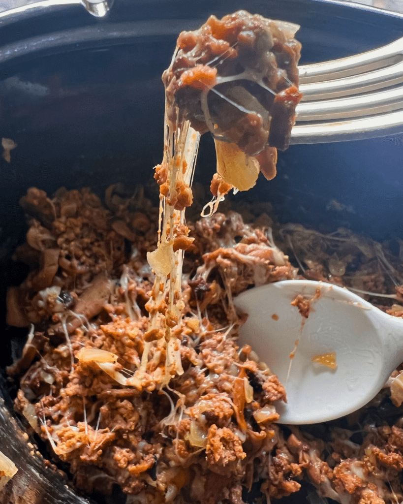 ground beef with onions, spices and lots of cheese on a fork over a slow cooker