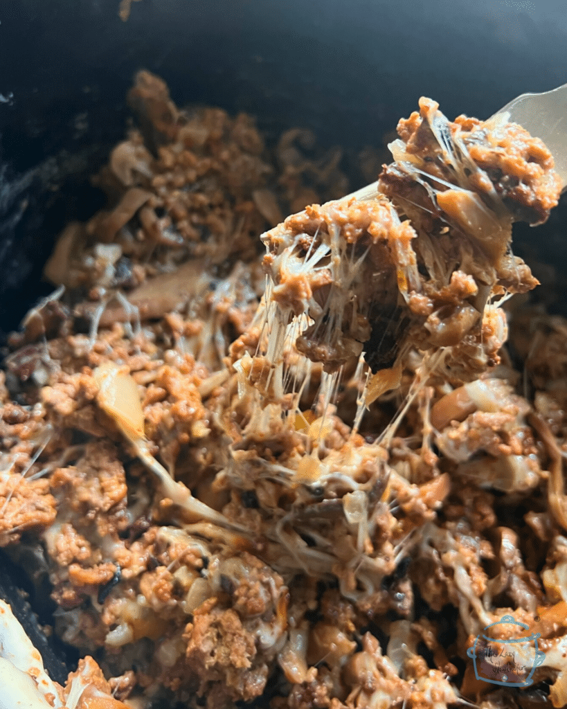 ground beef with onions, spices and lots of cheese on a fork over a slow cooker