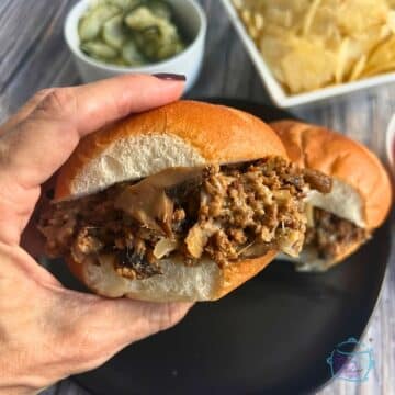 slow cooker cheesesteak sloppy joes on a bun held up in the air by a hand