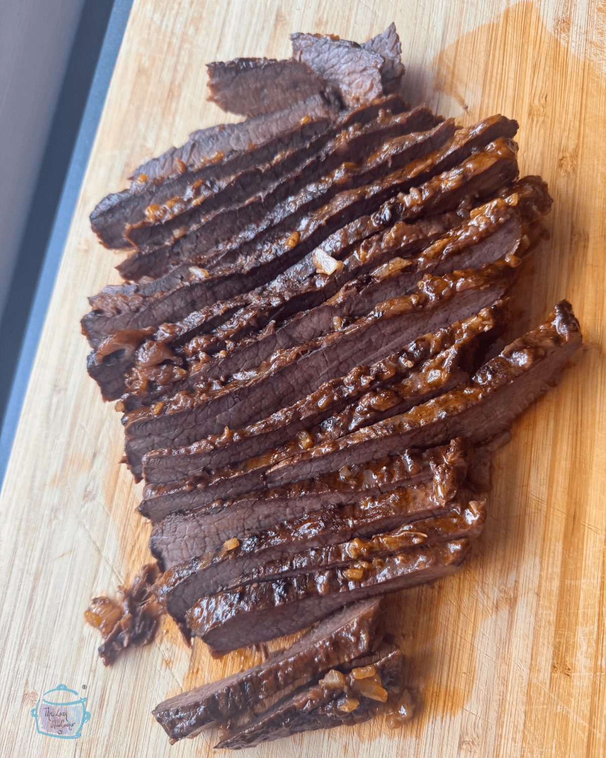 Slices of slow-cooked brisket are laid out on a wooden cutting board, displaying moist, tender meat with a shiny brown glaze.