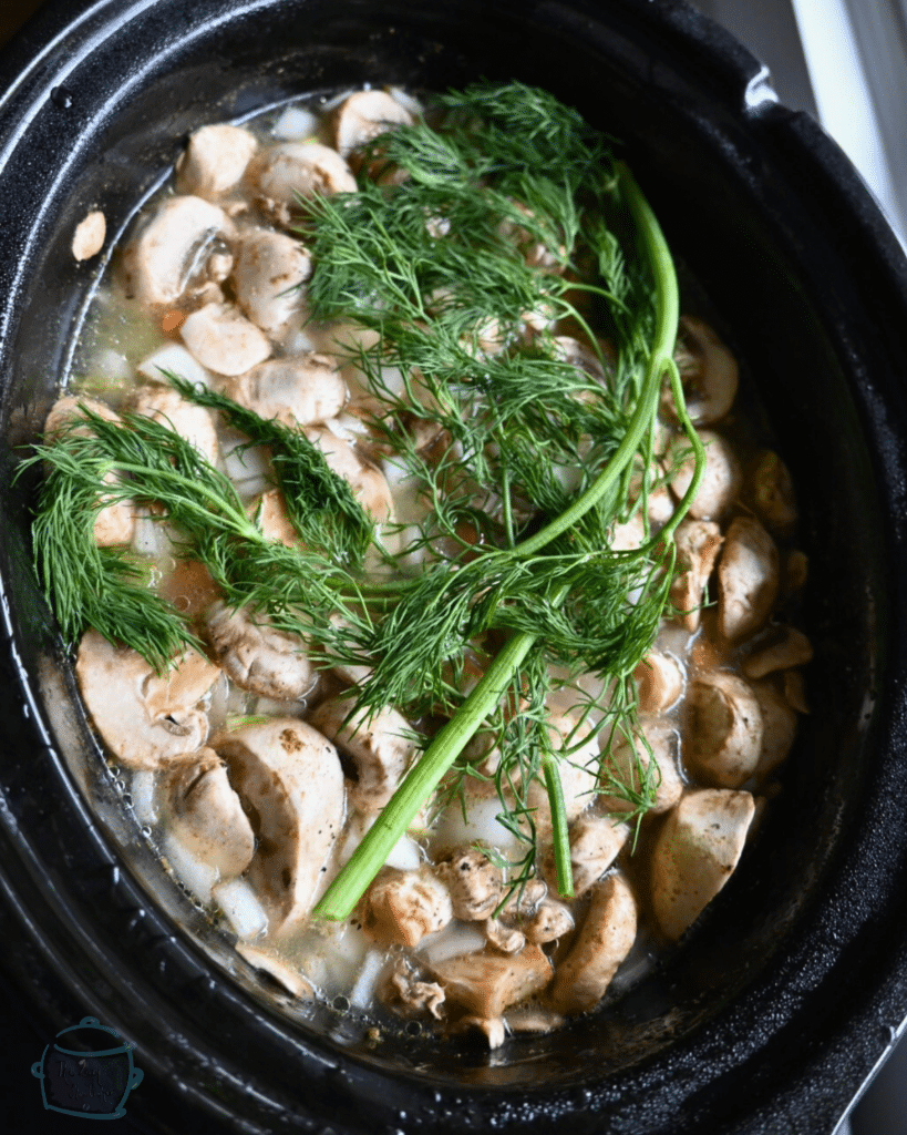 vegetables and broth topped with a dill branch in a slow cooker pot
