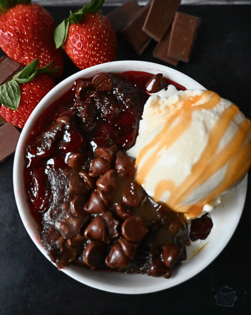 a bowl full of chocolate strawberry crockpot brownie with a scoop of vanilla ice cream drizzled with caramel sauce.