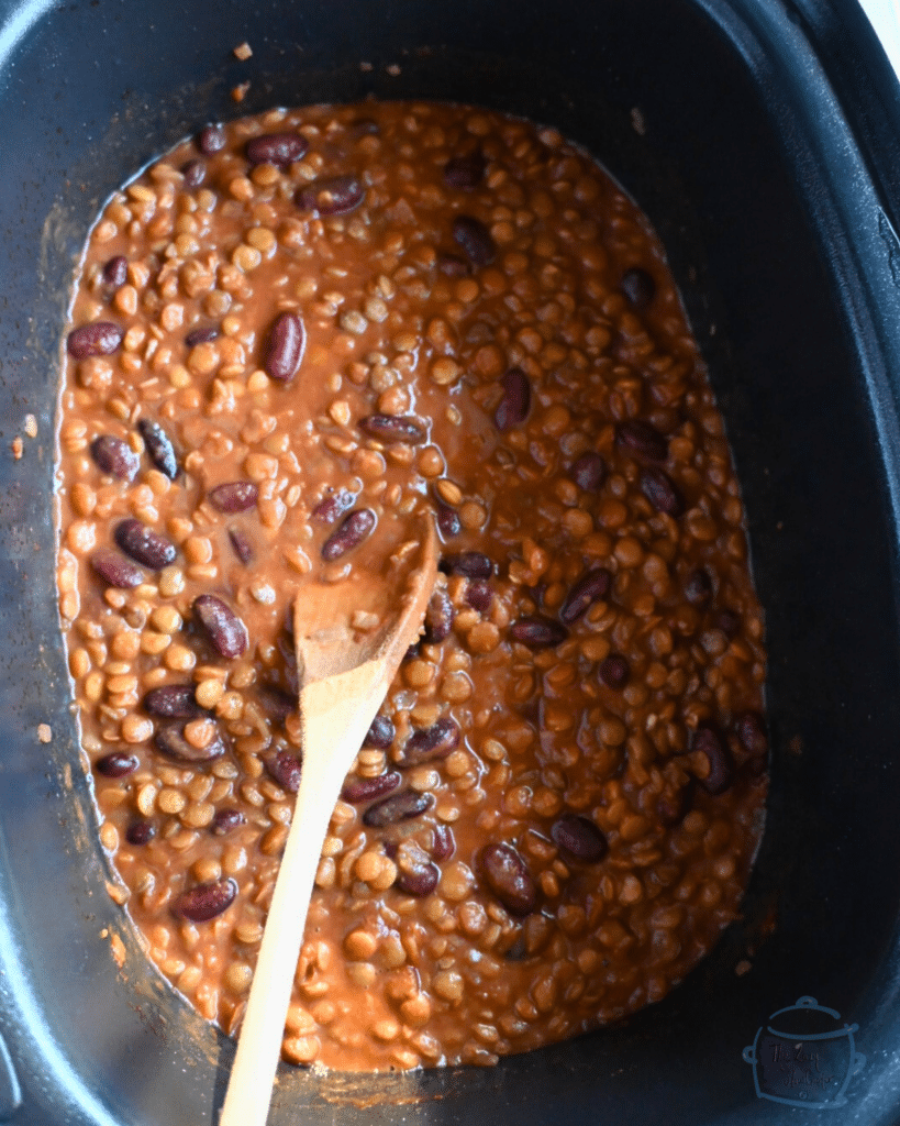 Cooked lentils and beans in slow cooker with a wooden spoon