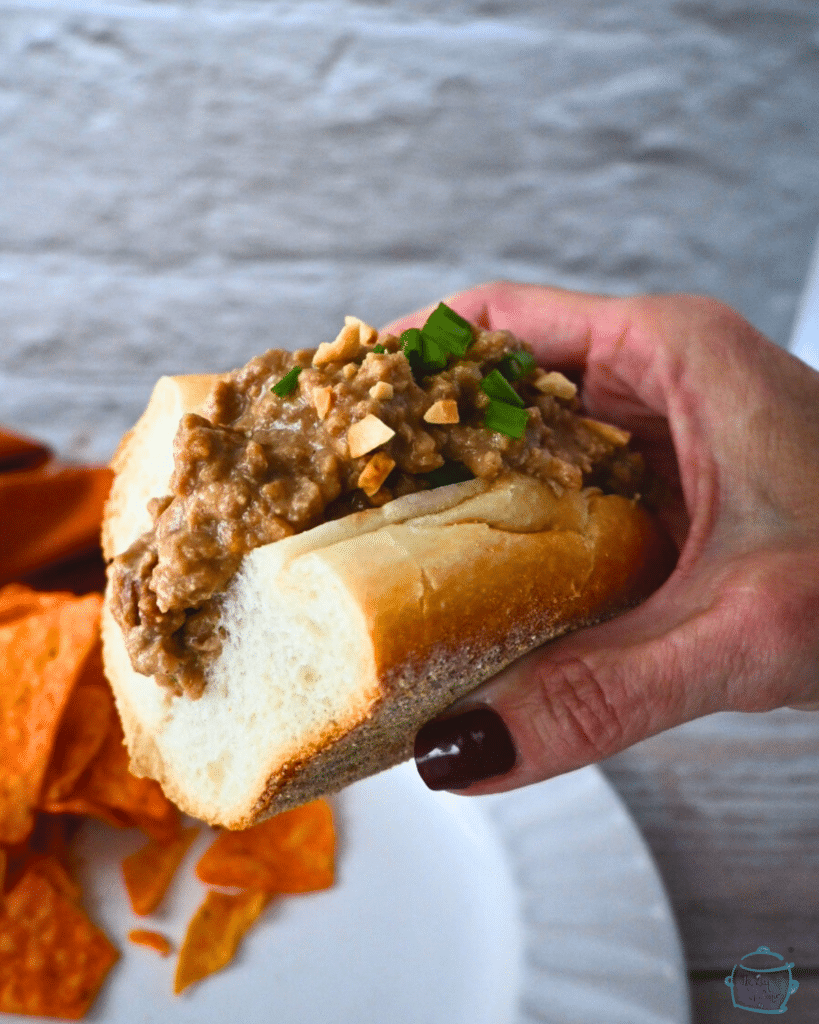 slow cooker ground chicken satay on a roll held by a hand