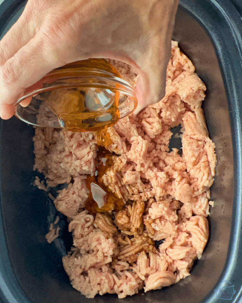 Adding satay ingredients into slow cooker over ground chicken