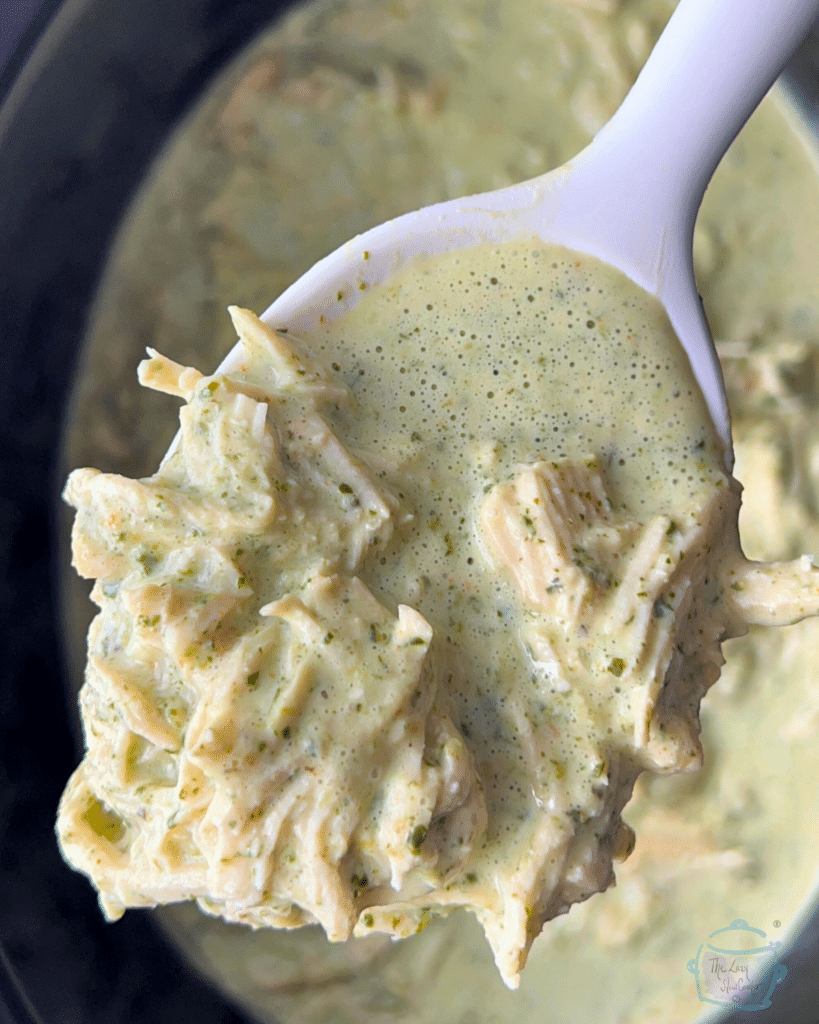 Creamy cilantro chicken held in a spoon over a crockpot crock full of the same.