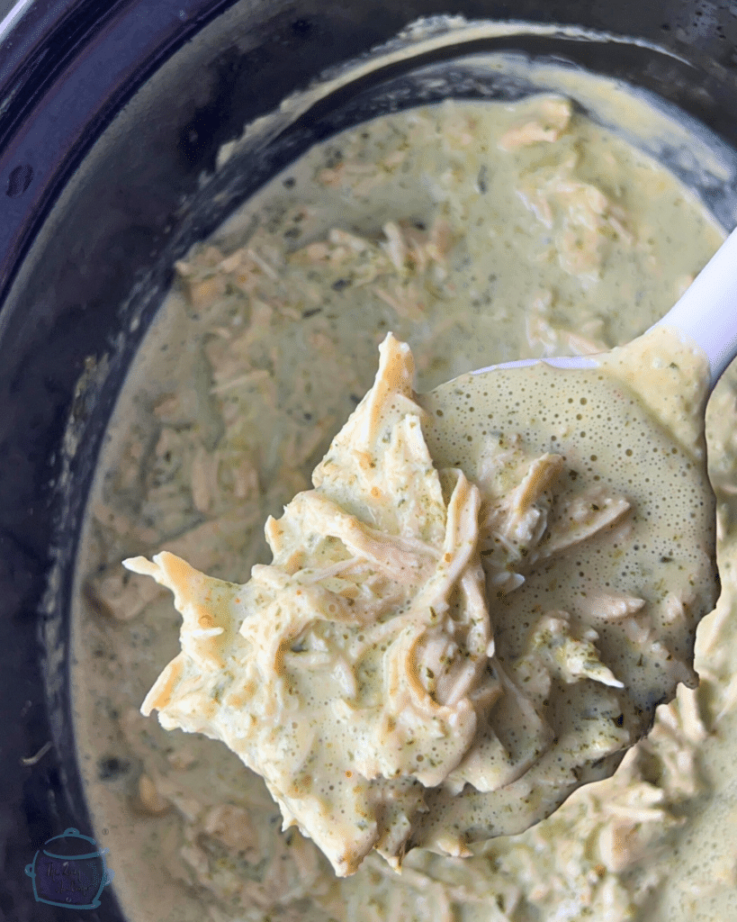 Creamy cilantro chicken held in a spoon over a crockpot crock full of the same.