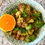 Orange beef and broccoli in a blue and white bowl with an orange off to the side