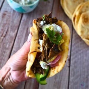 Shredded beef shawarma with toppings wrapped in pita held in a hand