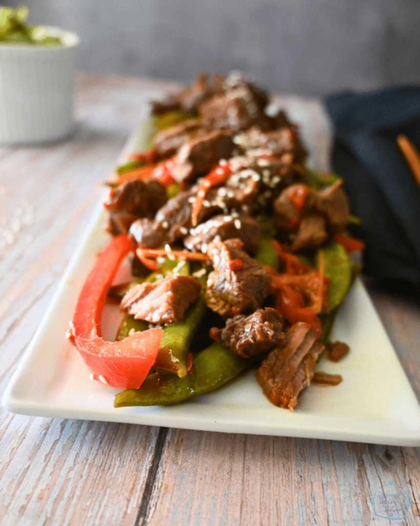 a side view of a long white tray with beef, sugar snap peas and red peppers
