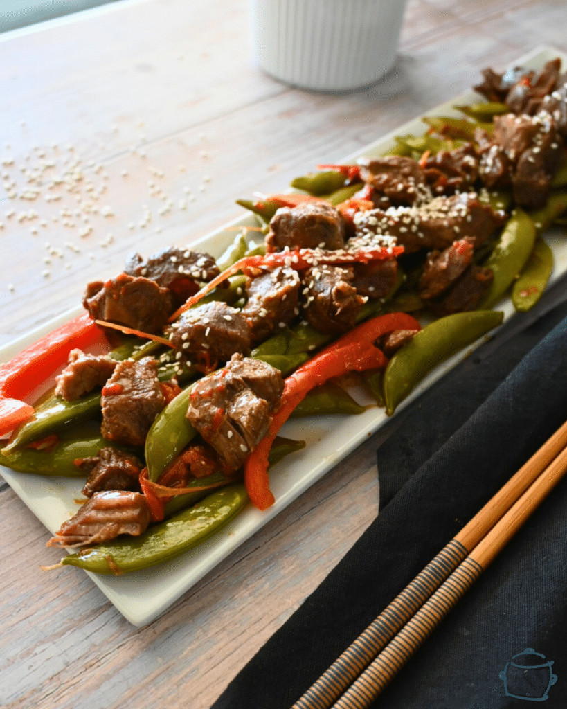 a side view of a long white tray with beef, sugar snap peas and red peppers