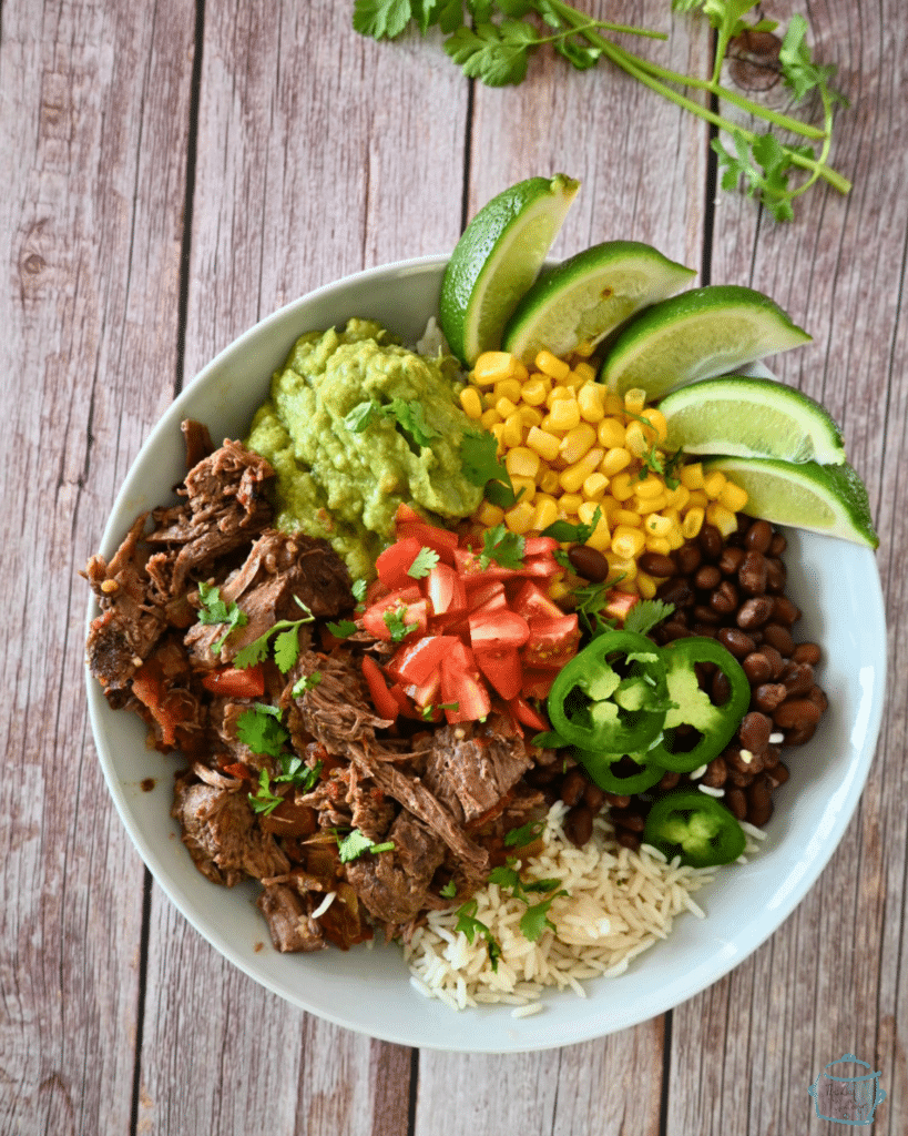 a plate of chipotle beef with corn beans tomatoes and lime wedges