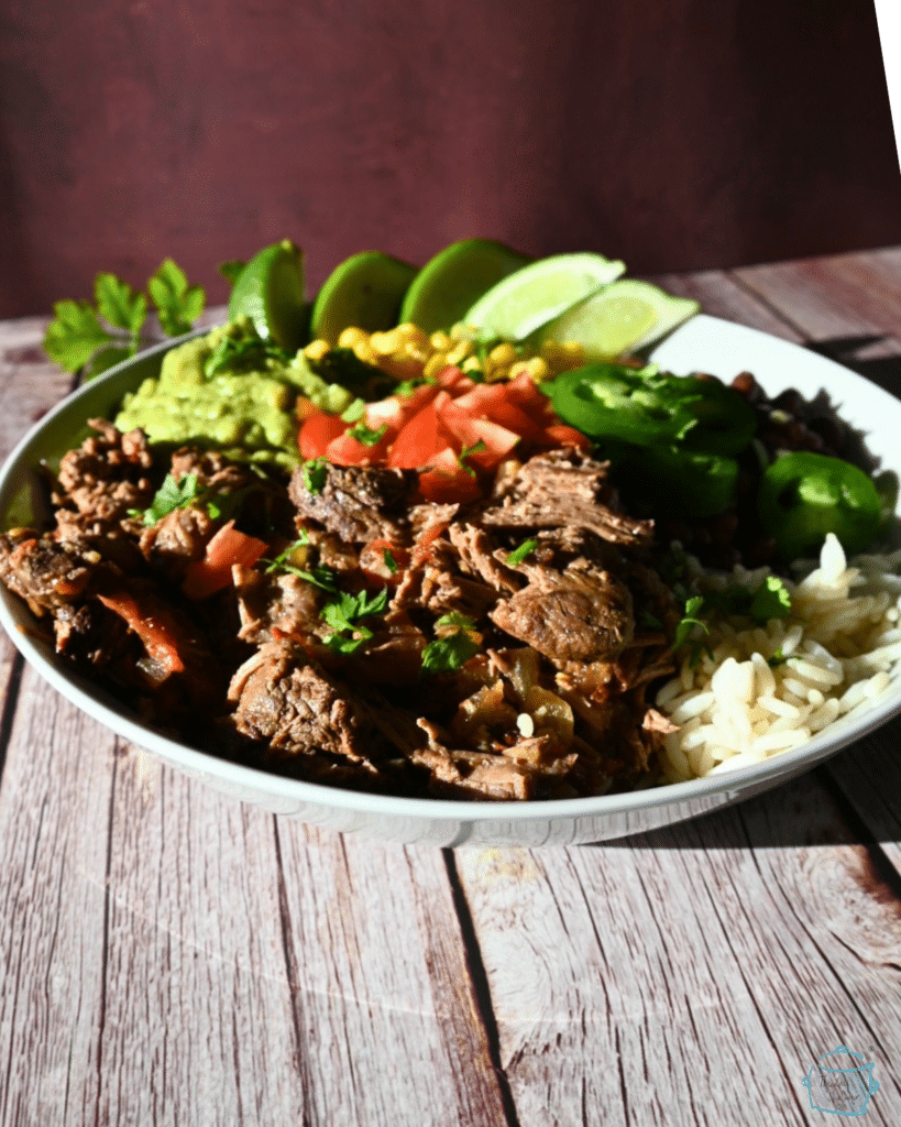 a plate of chipotle beef with corn beans tomatoes and lime wedges