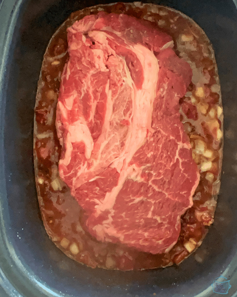 A whole chuck roast in a slow cooker with chipotle beef seasonings