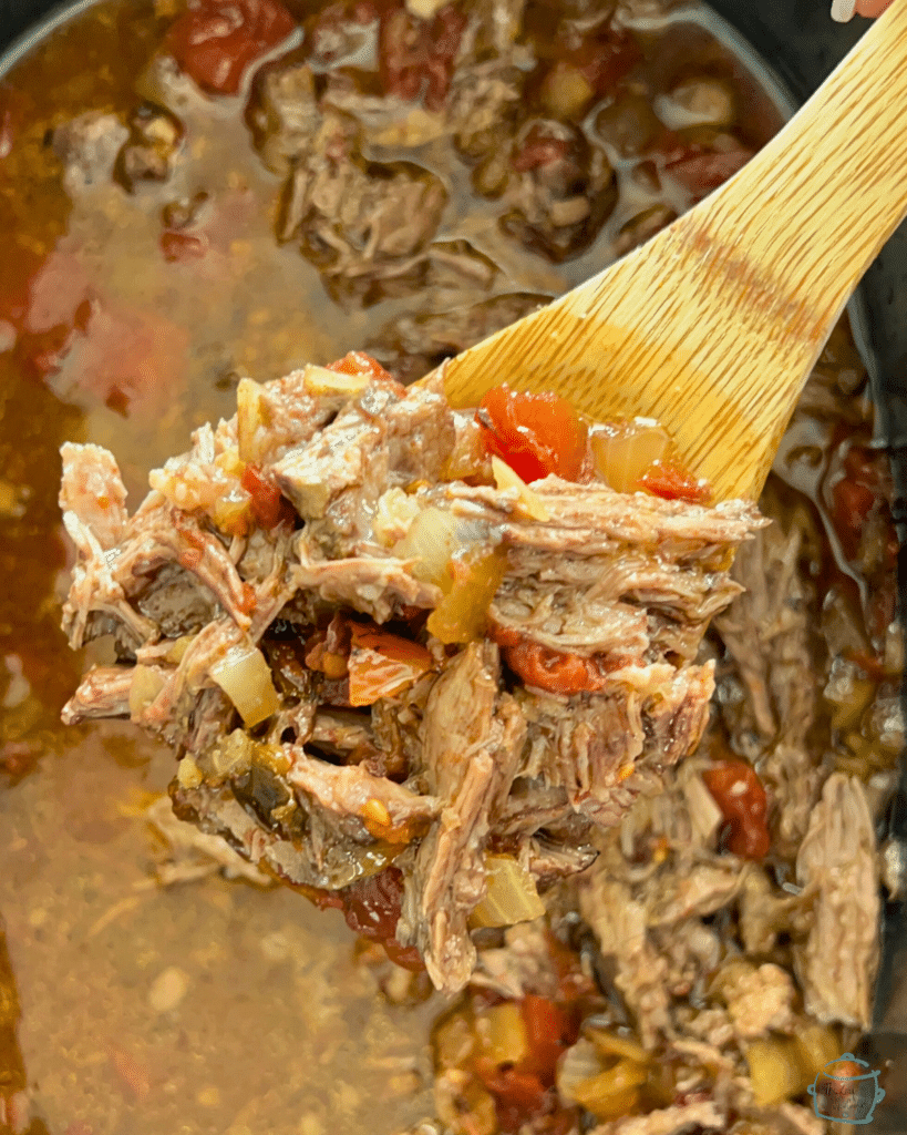 cooked and shredded beef that has been mixed back in with the chipotle seasonings held on a wooden spoon