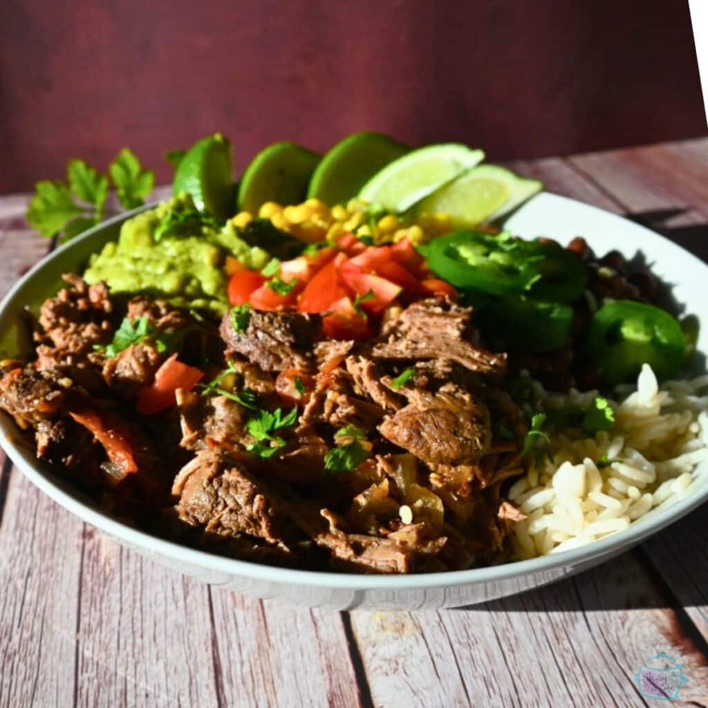 a plate of chipotle beef with corn beans tomatoes and lime wedges