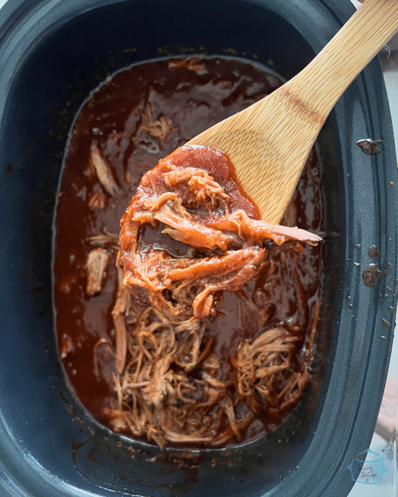 shredded bbq brisket on a wooden spoon held over a slow cooker full of the same.