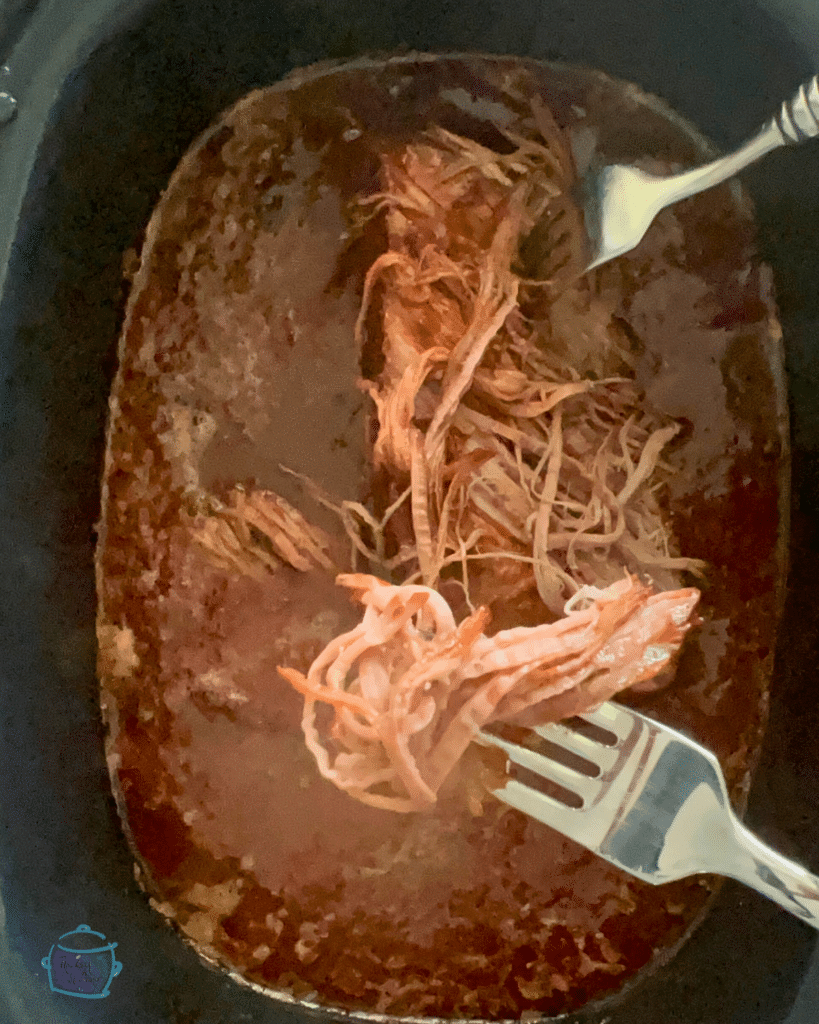 shredded beef in a slow cooker of bbq sauce with two forks