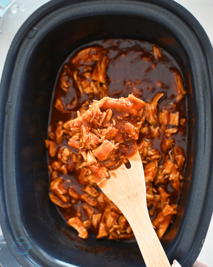 BBQ turkey tenderloin on a wooden spoon over a slow cooker full of the same.