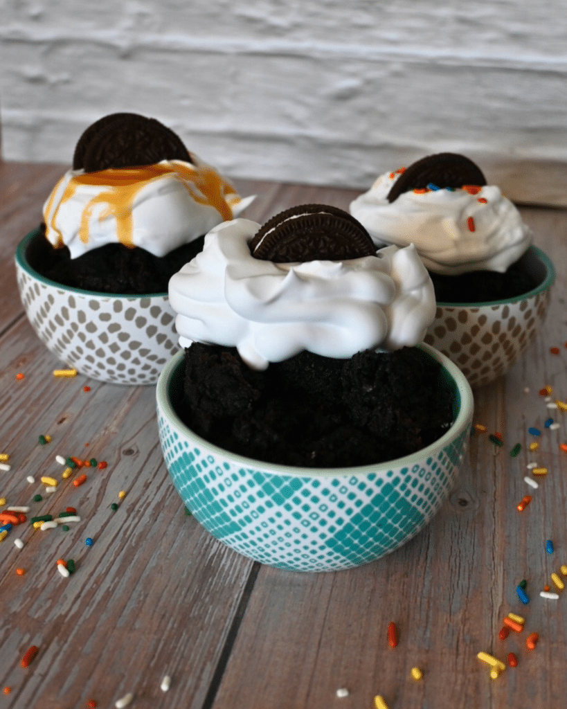 three bowls of oreo mug cake each with a different topping and half and oreo on top