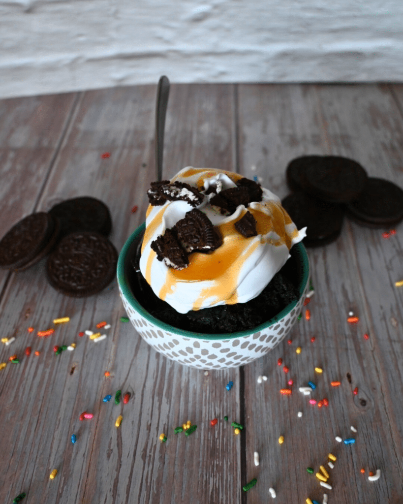 1 bowl of oreo mug cake with whipped cream, caramel sauce, sprinkles, and half and oreo on top