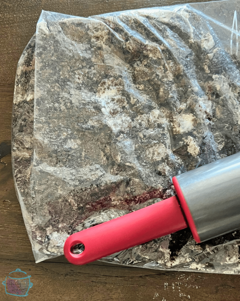 oreos in a plastic bag being crushed by a heavy rolling pin