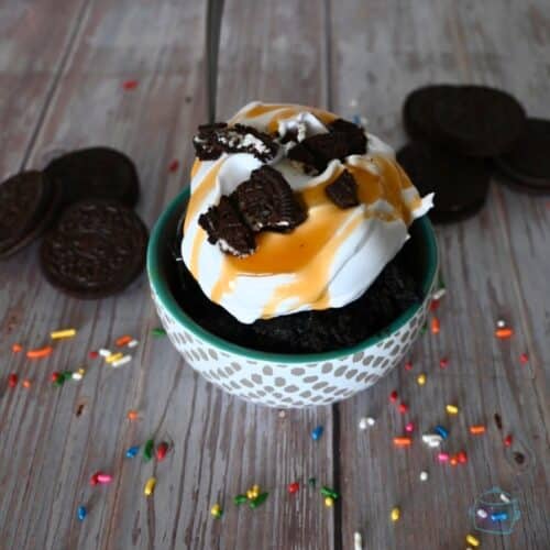 1 bowl of oreo mug cake with whipped cream, caramel sauce sprinkles, and half and oreo on top