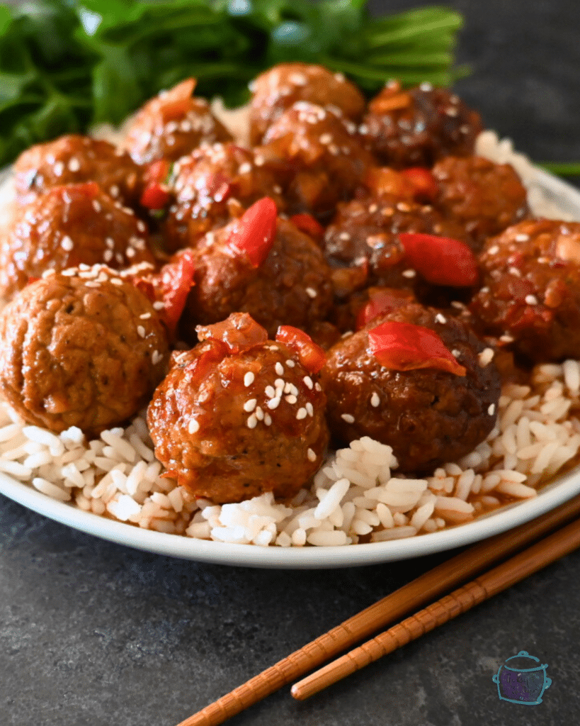 a close up of meatballs on a bed of rice topped with red peppers