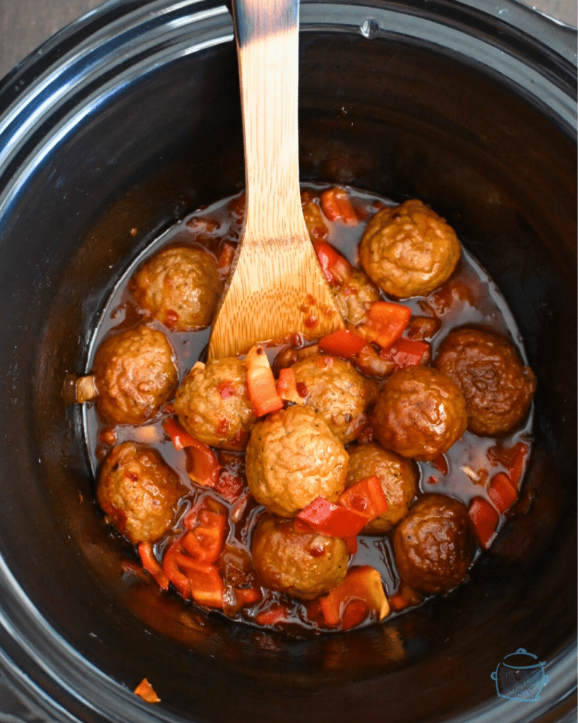 finished meatballs in slow cooker with a wooden spoon