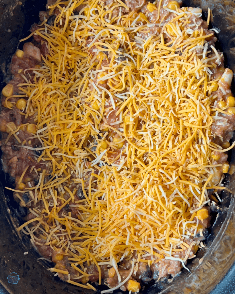 A slow cooker fully of tortilla lasagna topped with shredded cheese