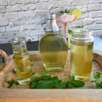 three different glass jars on a try containing mint simple syrup